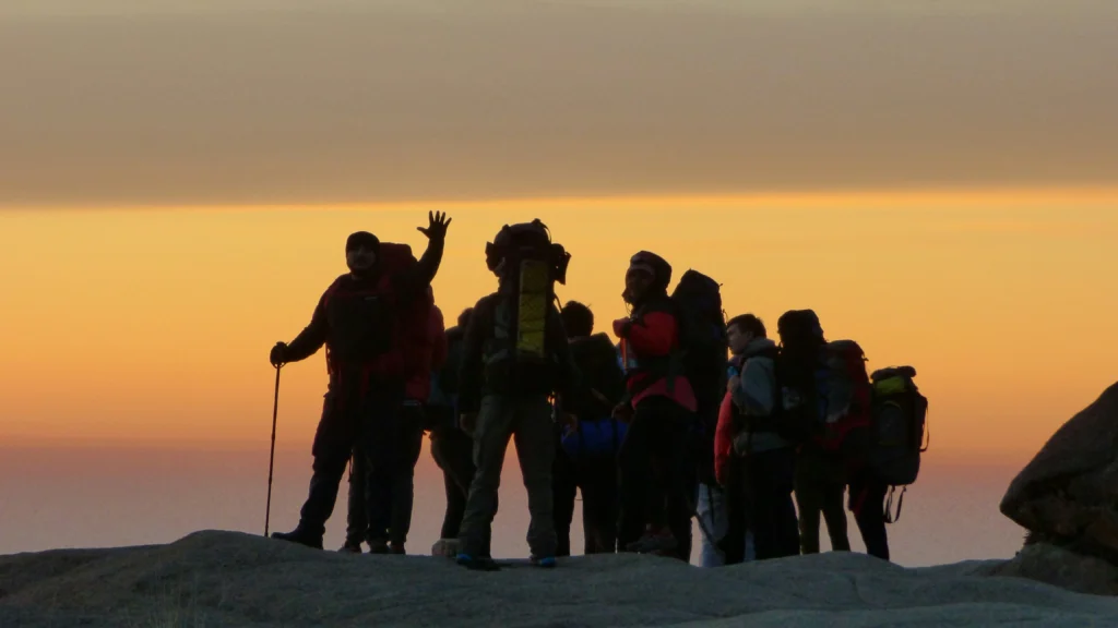 Silhouetted leaders standing on a mountain peak at sunrise, symbolizing vision.